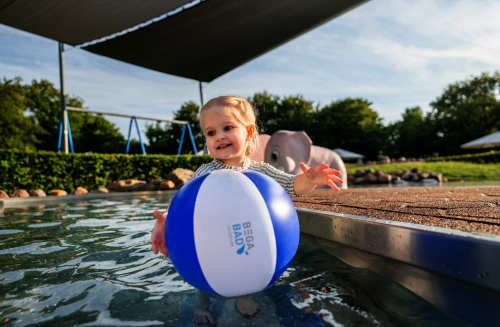 Kleines Mädchen im Kinderbecken mit Wasserball