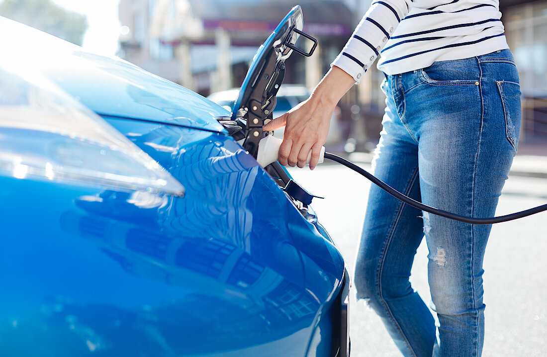 Person steckt den Ladestecker in ein blaues Auto