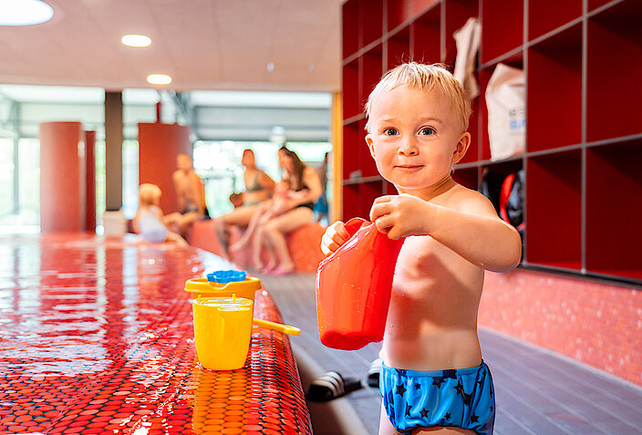 Ein kleiner Junge spielt mit einer Gießkanne am Planschbecken im Lohfeld