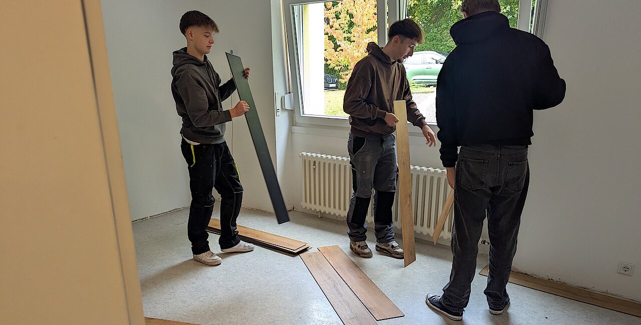 Drei Auszubildende verlegen Laminat für die Verschönerung des Lohfeld Treffs vom Pro Regio e.V.